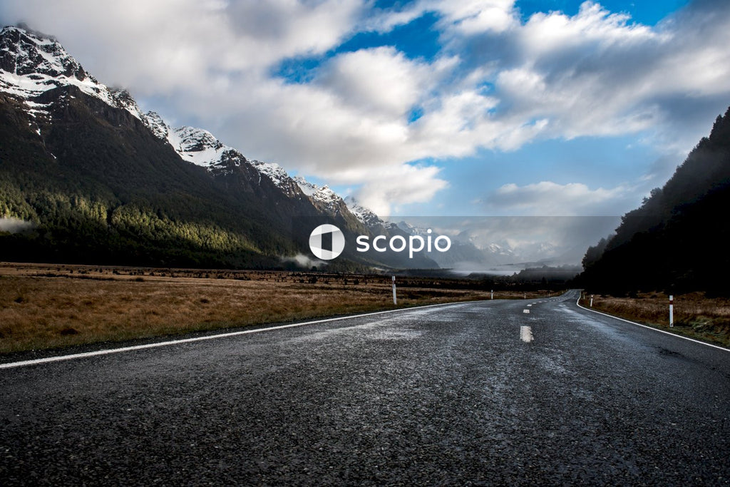 Gray asphalt road near mountain under white clouds
