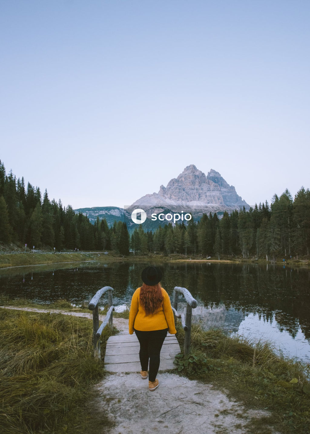 Woman in white long sleeve shirt and black pants standing on green grass field near lake