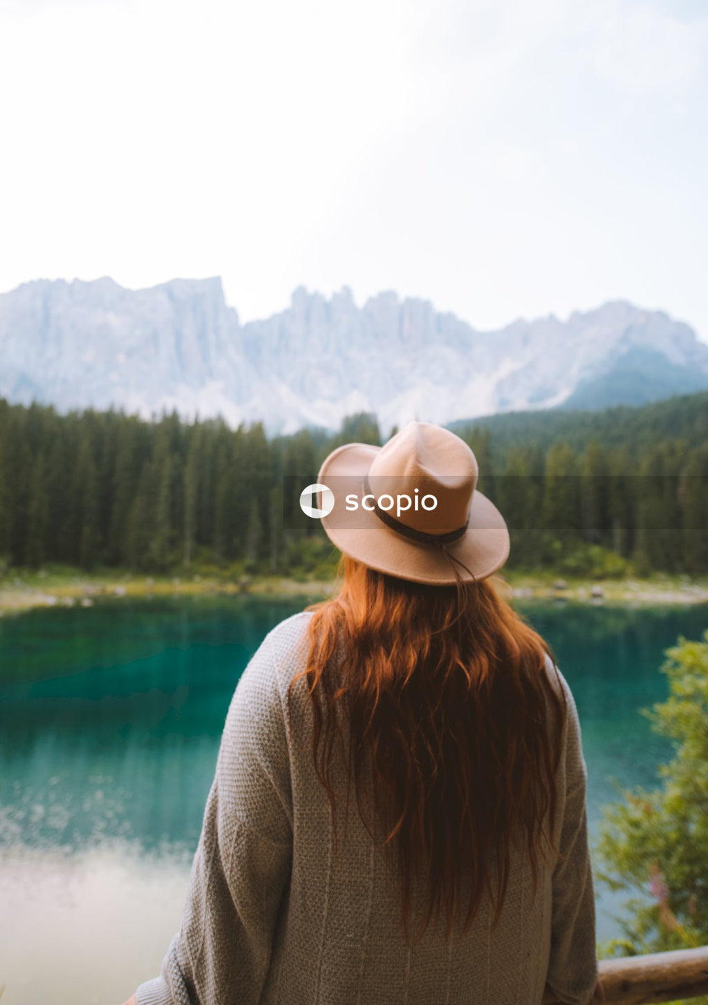 Woman in gray sweater wearing white fedora hat standing near lake