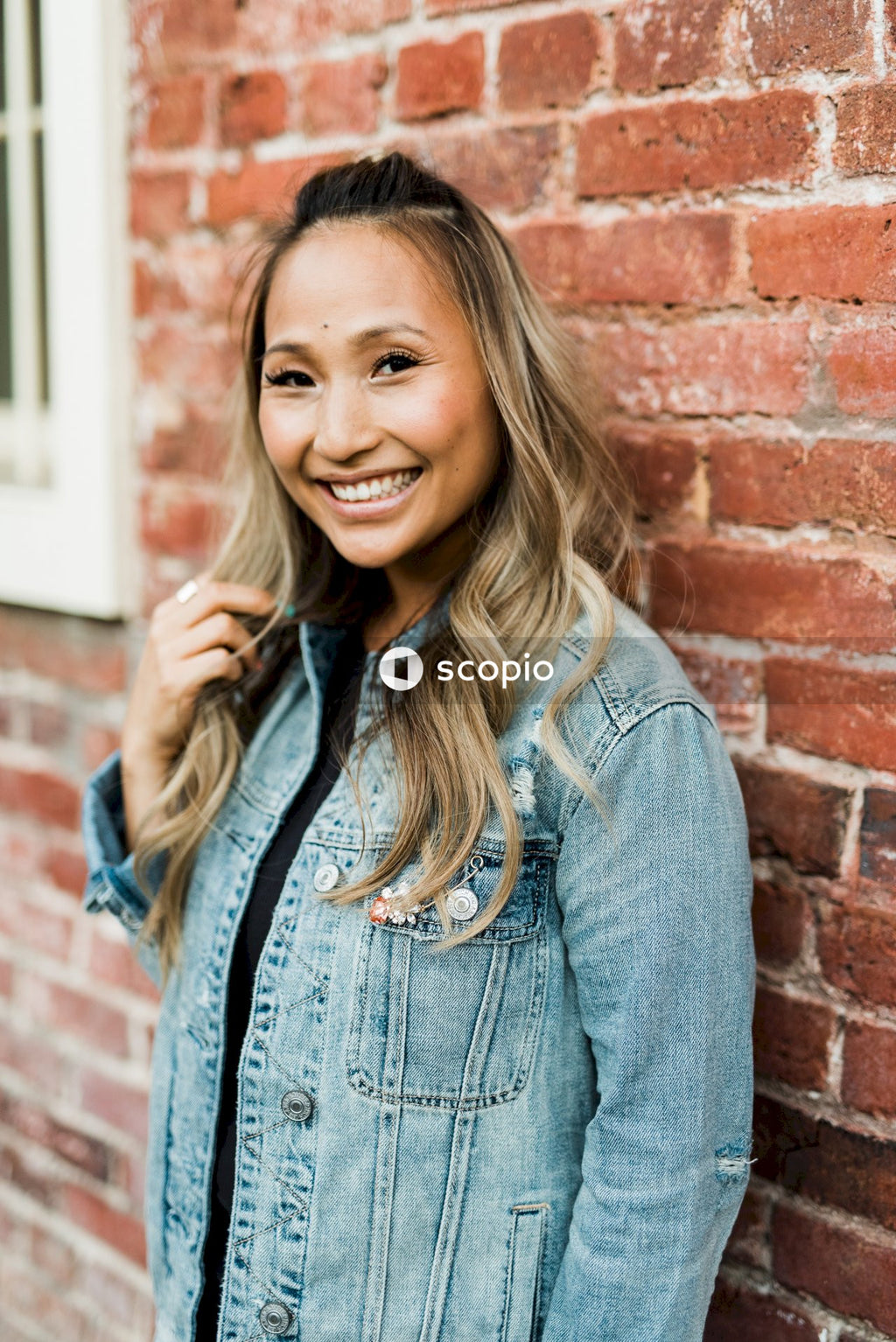 Smiling woman in blue denim jacket standing beside brick wall