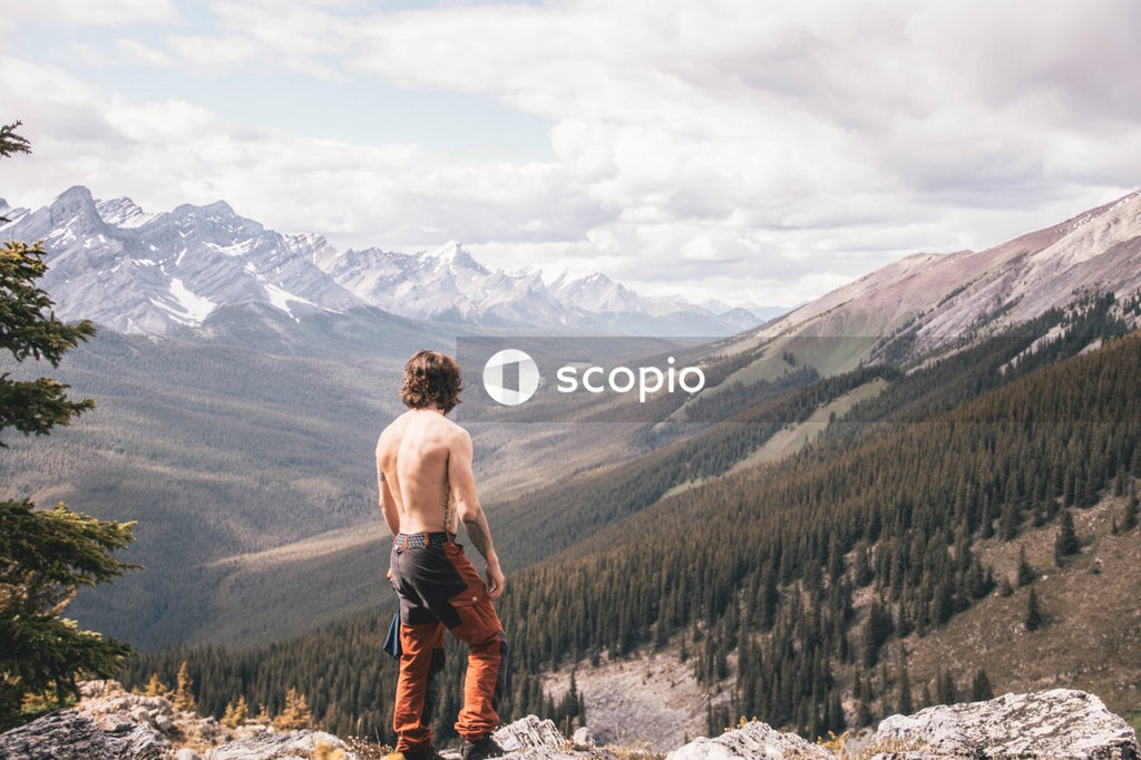 Man in White Shirt and Brown Pants Standing on Rocky Mountain