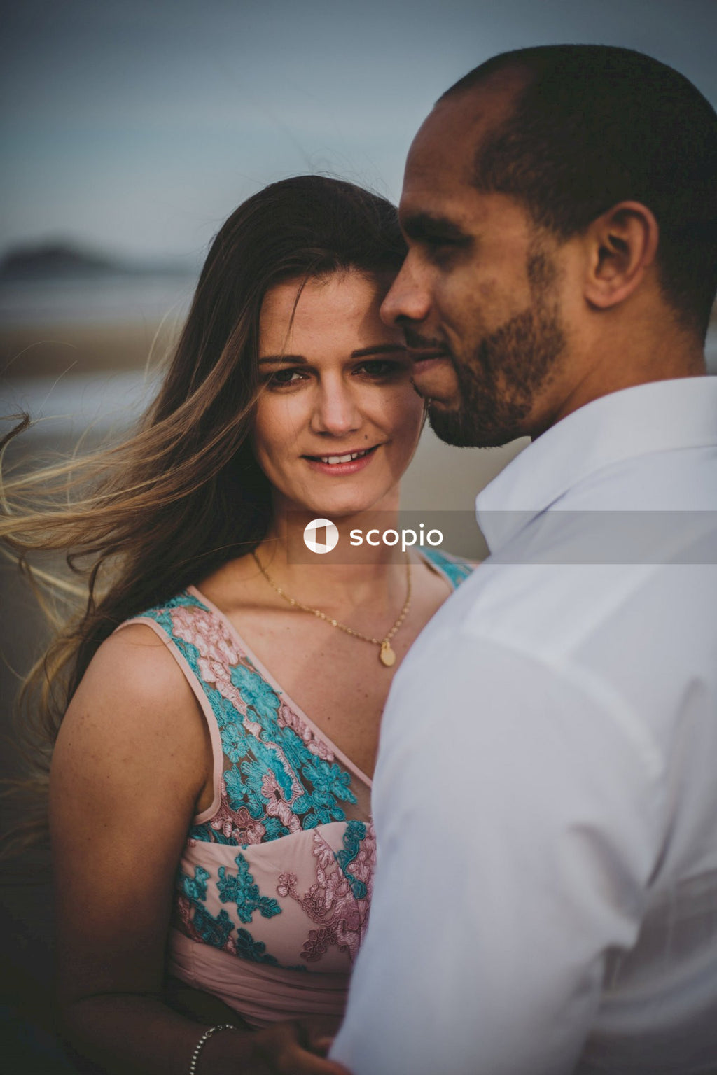 Man in white dress shirt kissing woman in white green and red floral sleeveless dress