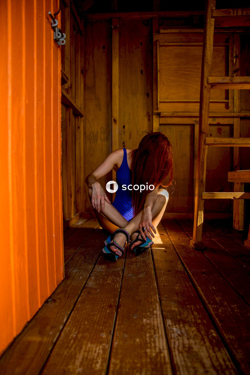 Woman in blue tank top sitting on brown wooden floor
