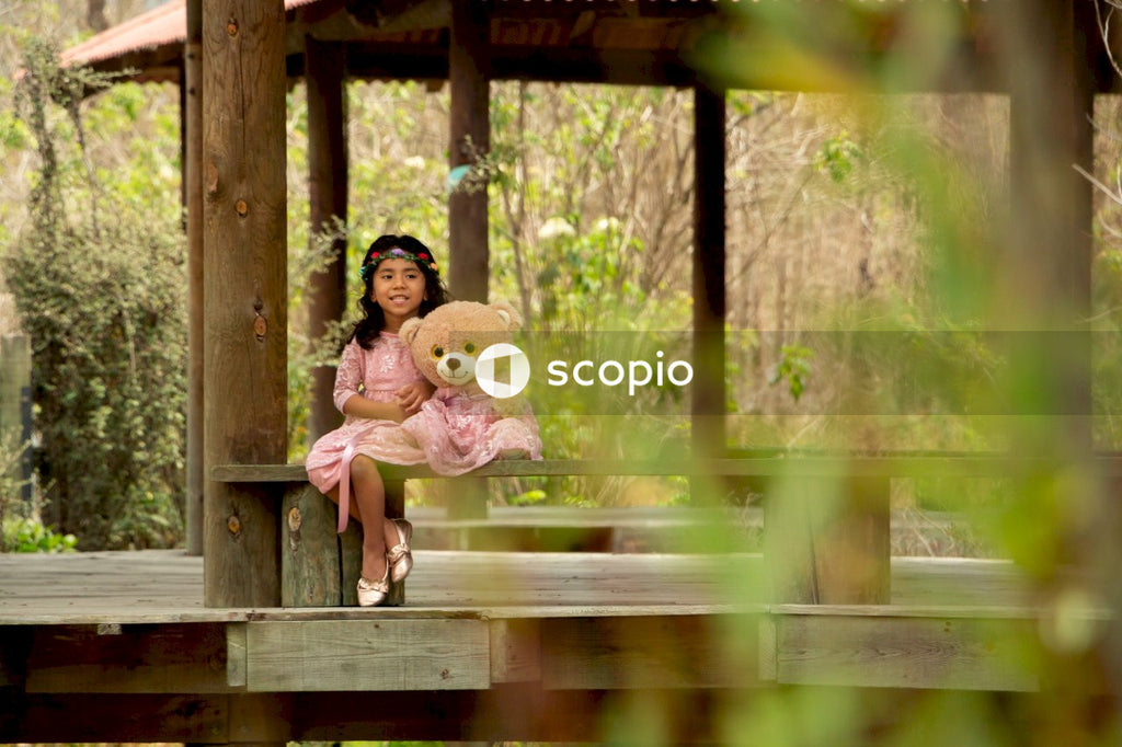 Girl in pink dress hugging girl in pink dress on brown wooden bridge