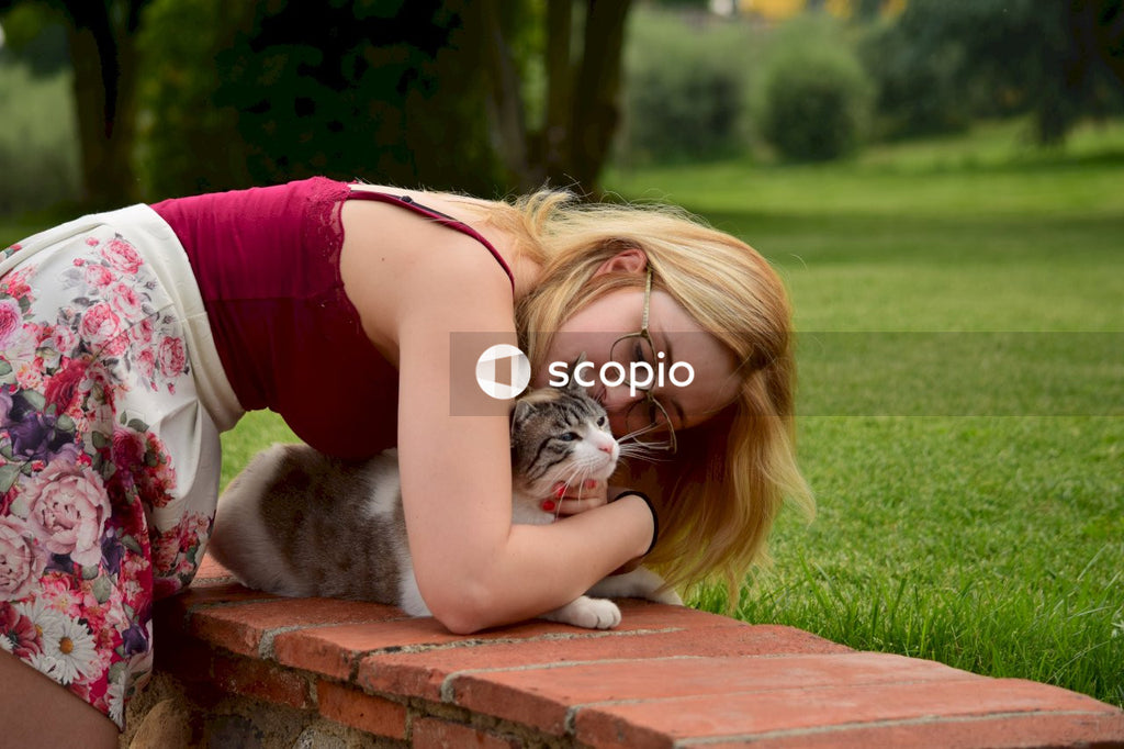 Girl in pink tank top hugging gray and white cat on brown wooden bench
