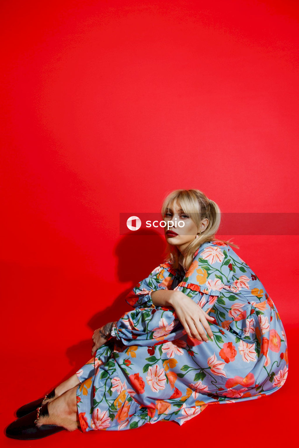 Girl in red and blue floral dress leaning on red wall