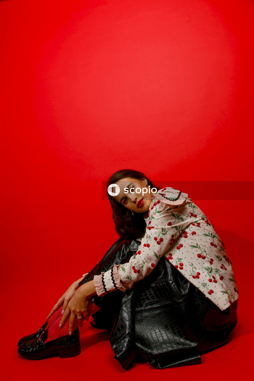 Girl in white and pink floral long sleeve shirt leaning on red wall