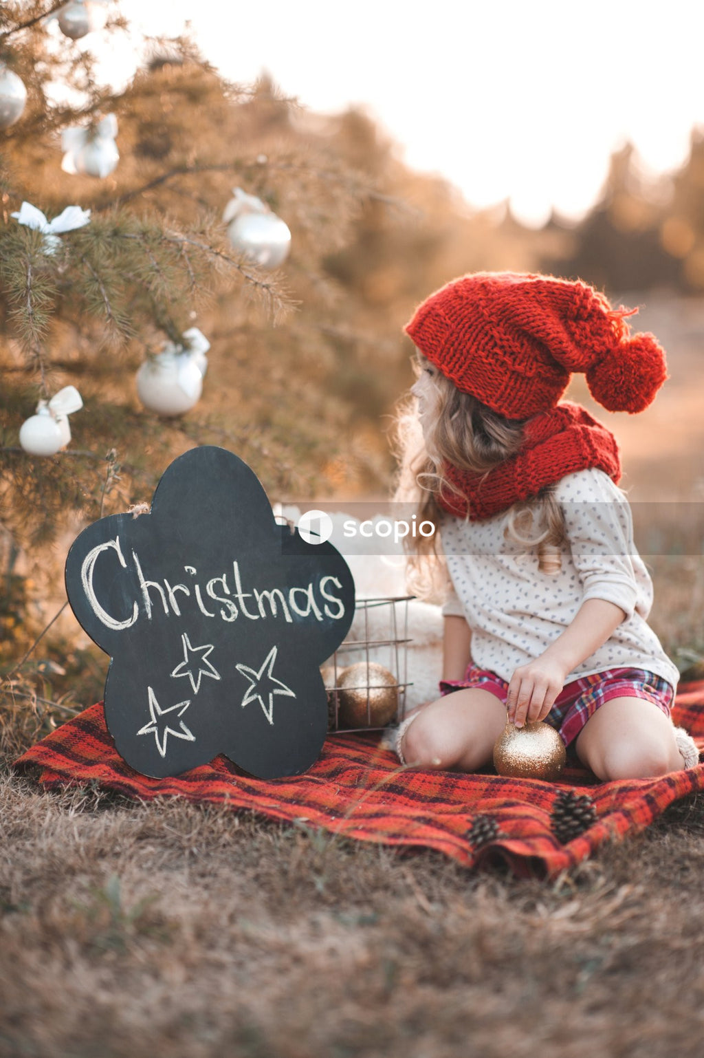 Girl in white long sleeve shirt and red knit cap sitting on red textile
