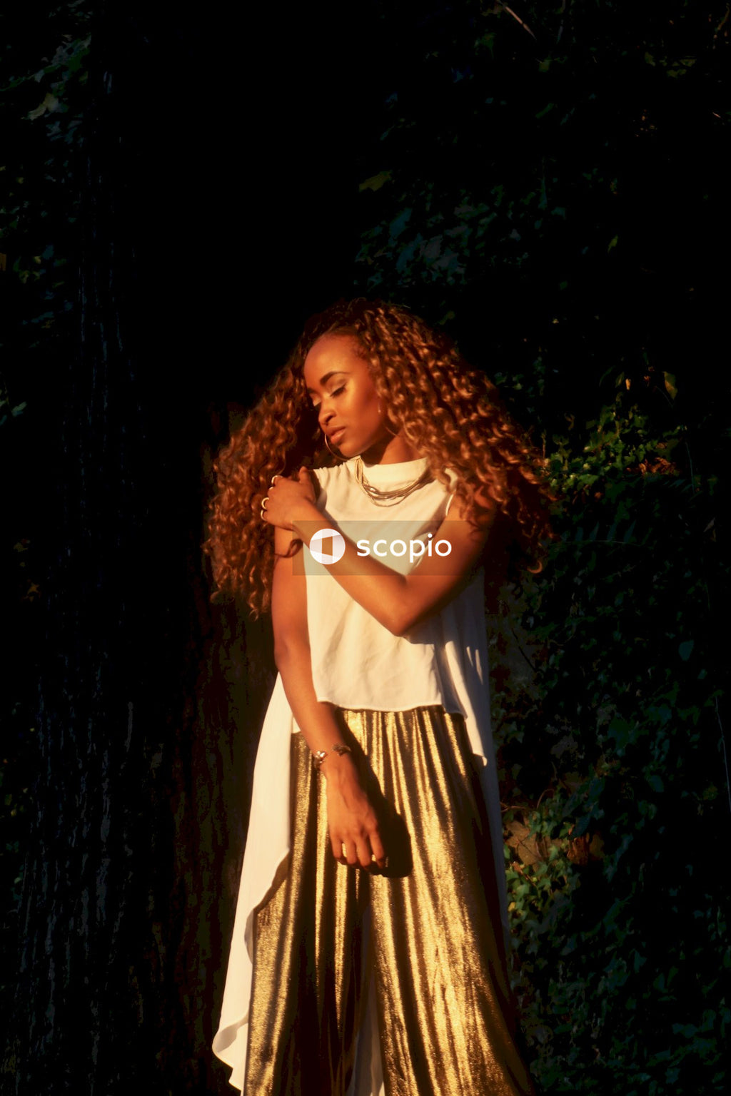 Girl in white t-shirt and brown skirt standing beside brown tree