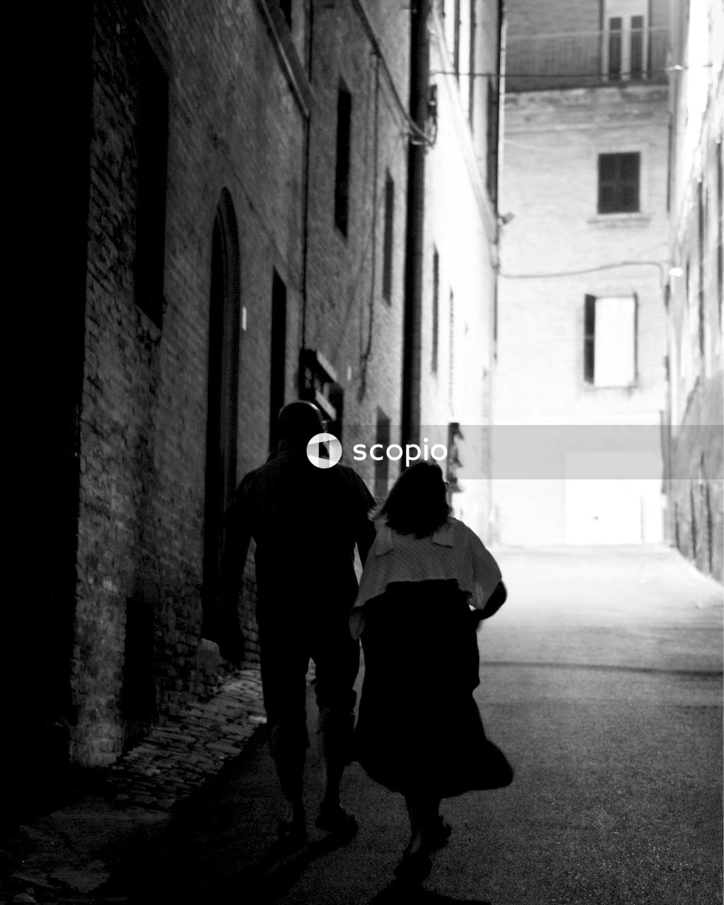 Grayscale photo of man and woman walking in an alley