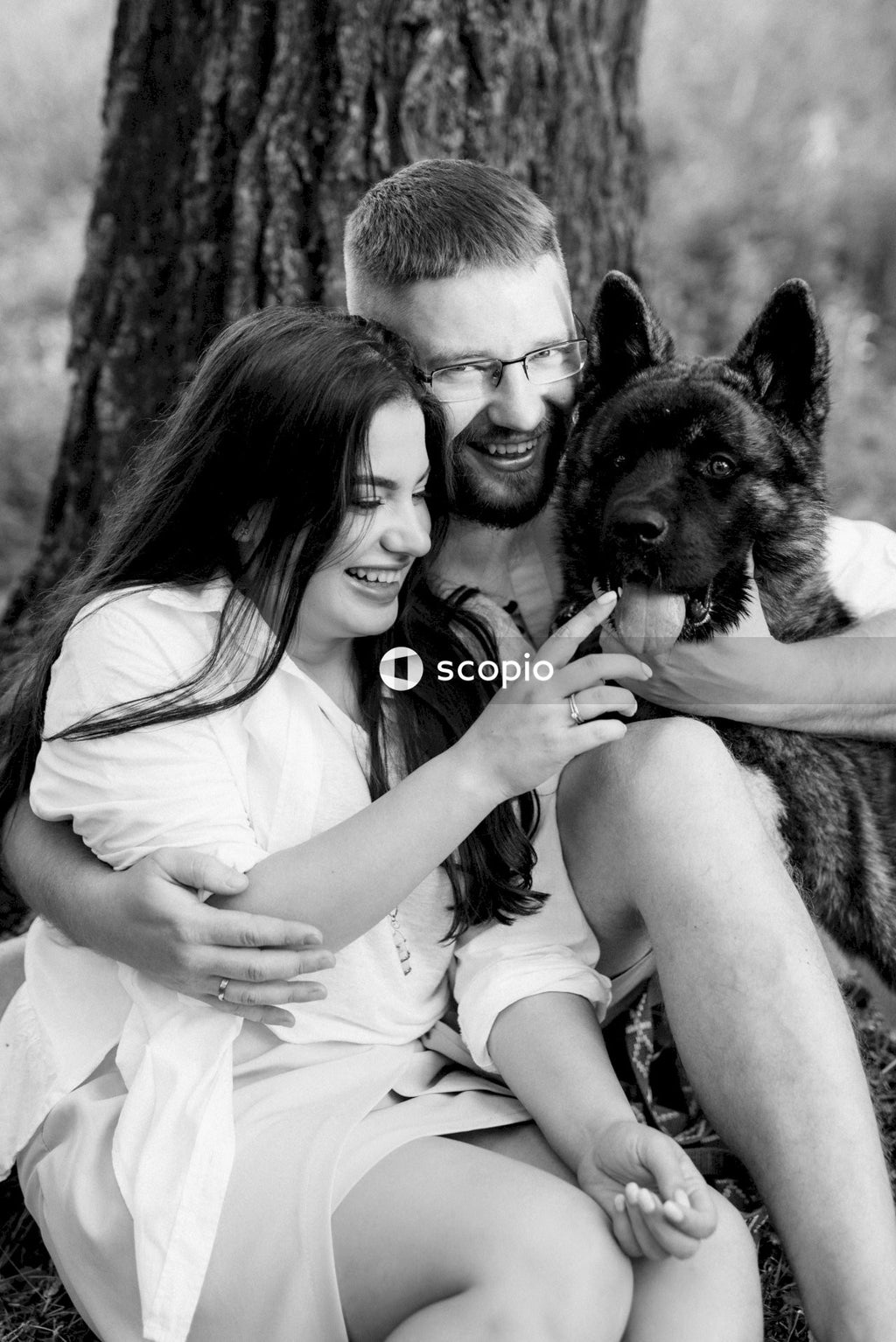 Grayscale photo of woman and man hugging a dog