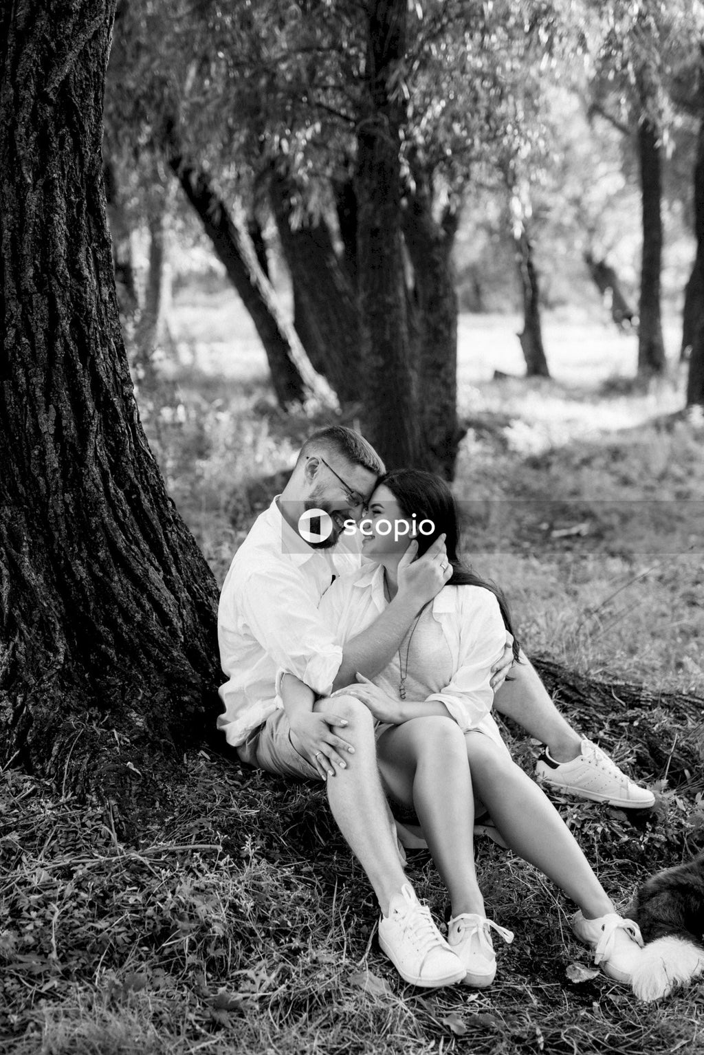 Grayscale photo of woman and man sitting beside tree