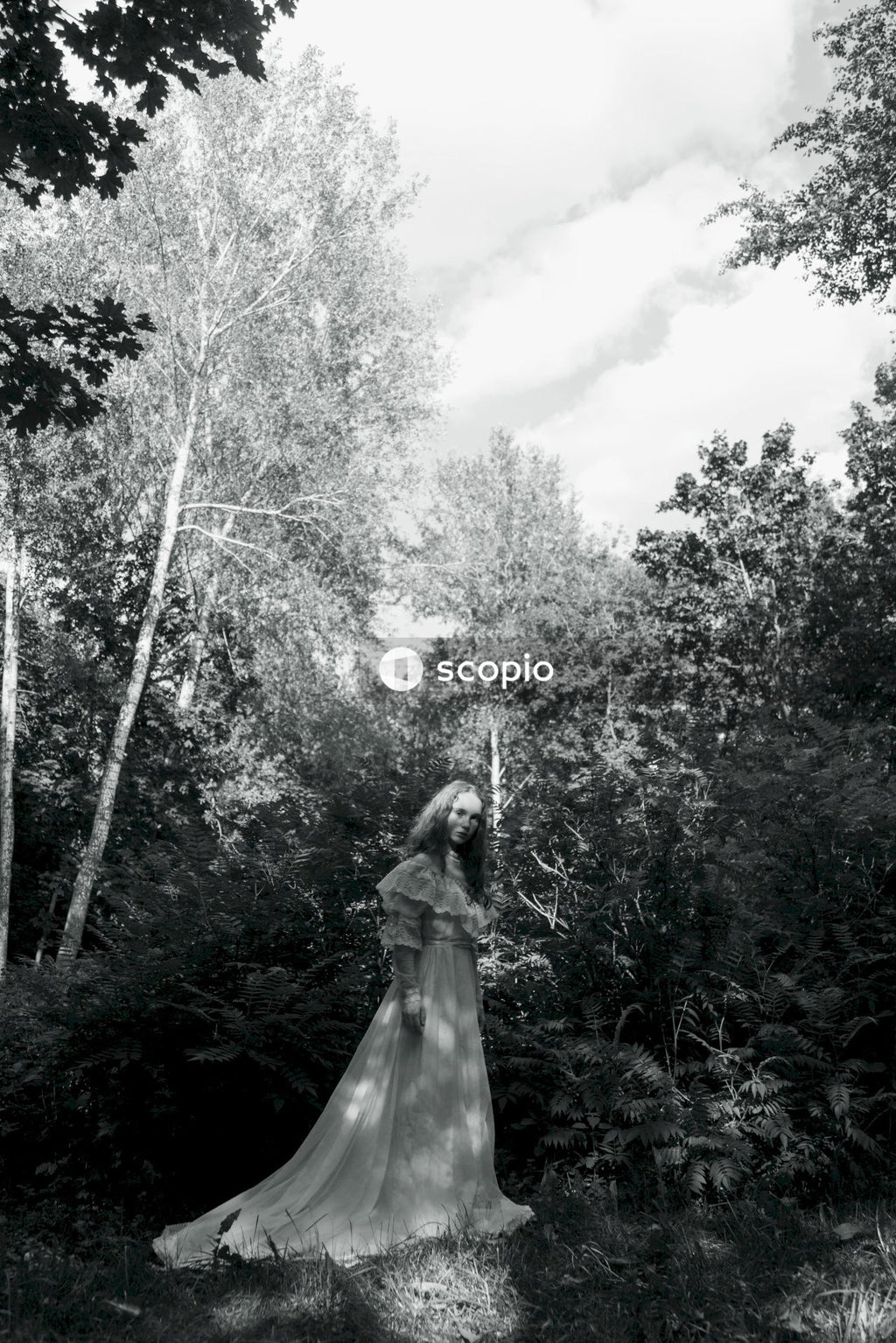 Grayscale photo of woman in dress standing on forest