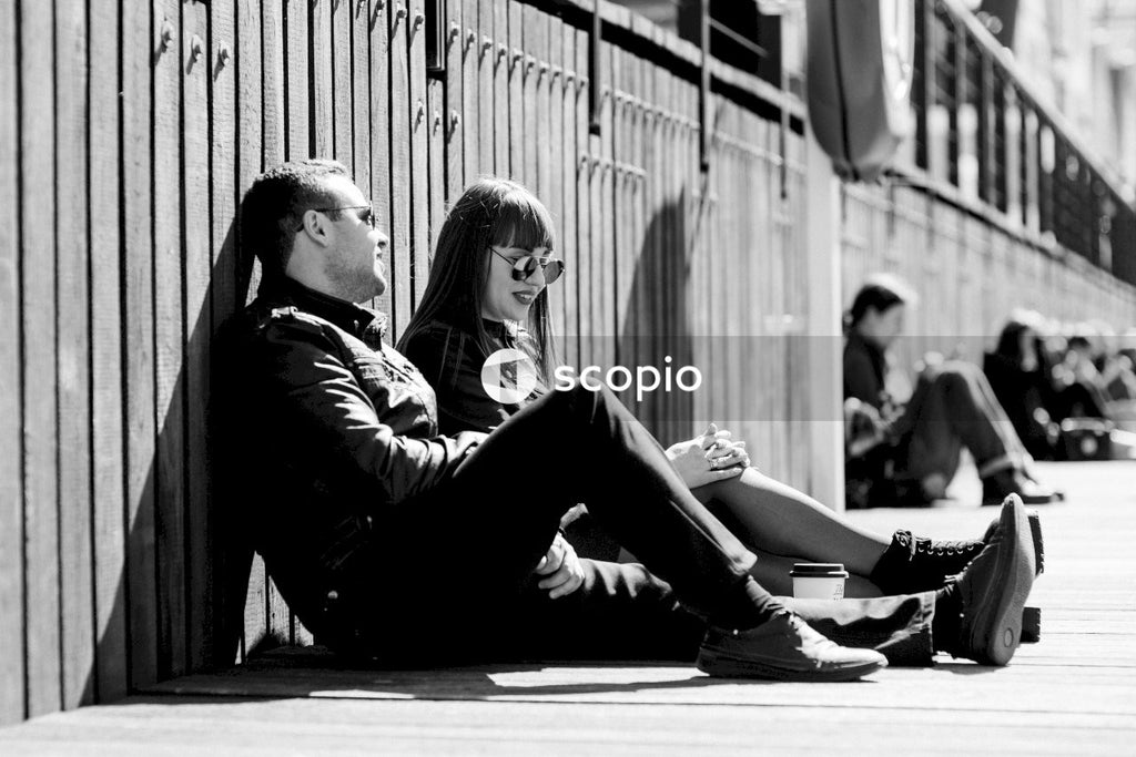 Grayscale photo of couple sitting on sidewalk outdoor in Gdansk, Poland