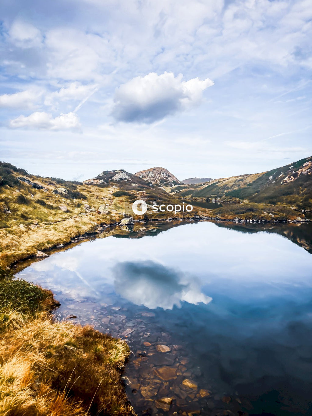Green and brown mountains beside river under white clouds and blue sky
