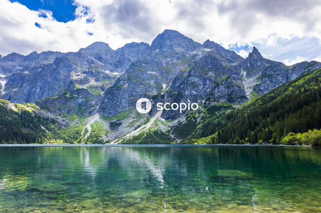 Green and gray mountain beside body of water under blue sky