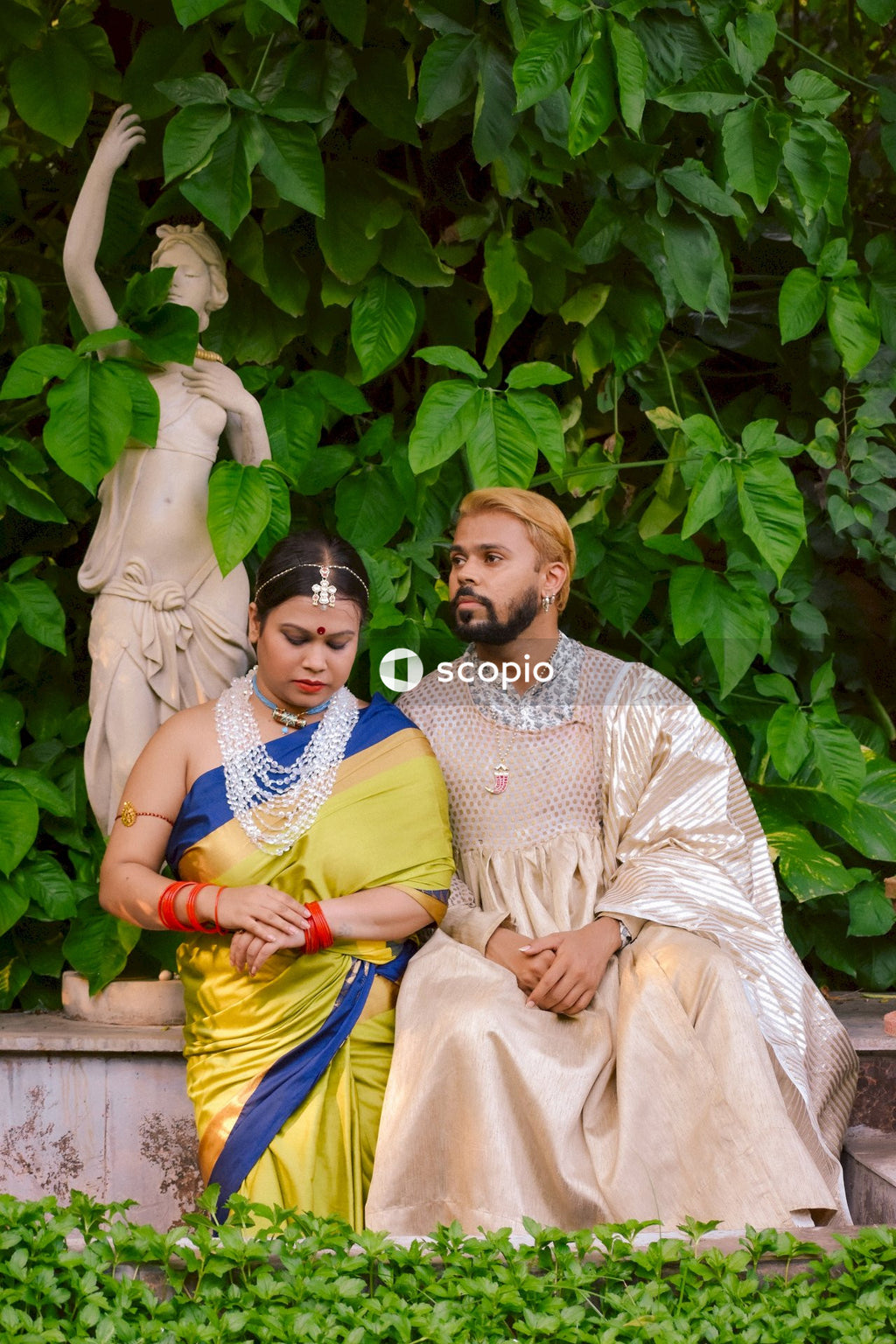 Indian man and woman sitting beside statue in a garden