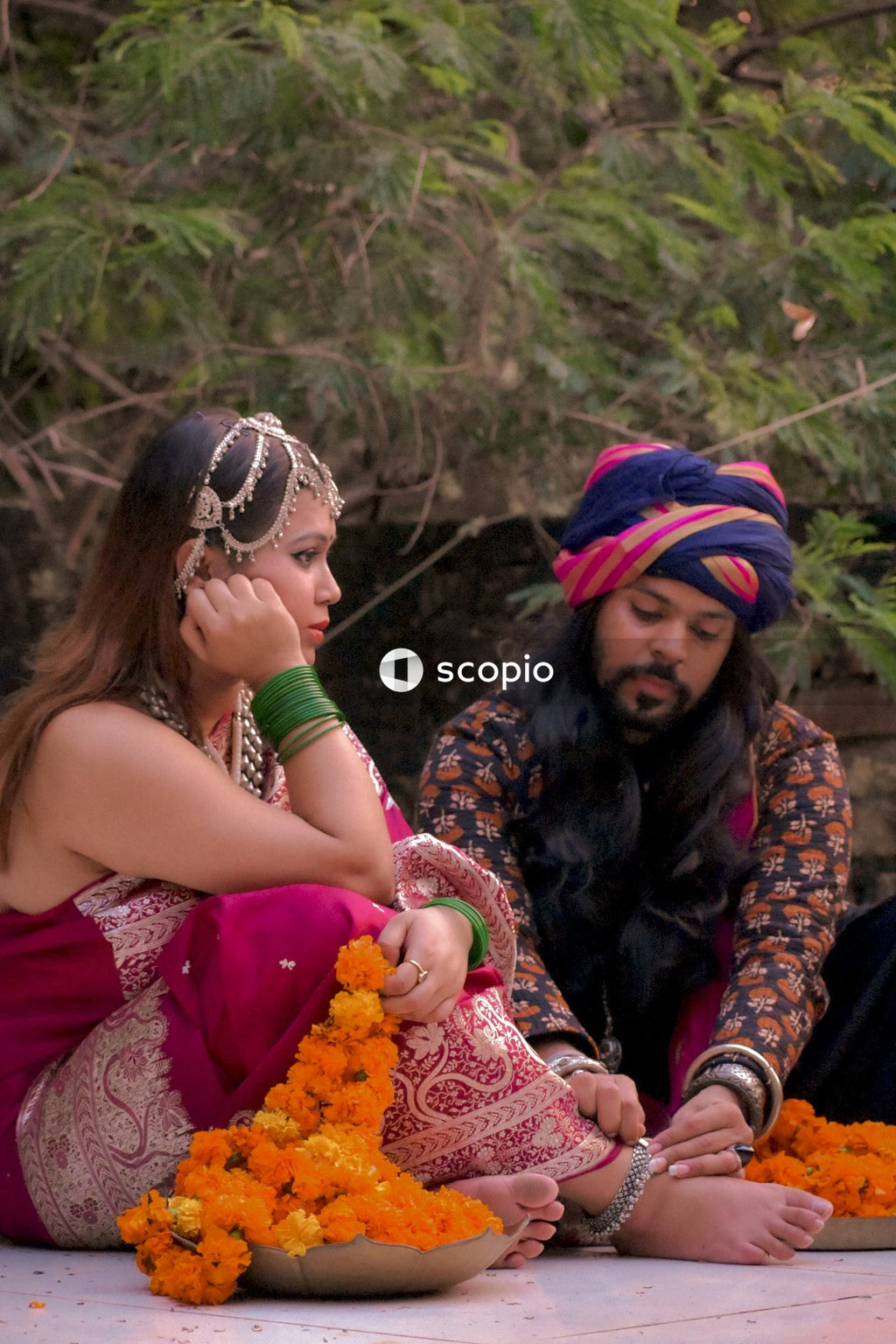 Indian man putting an anklet on woman's ankle sitting on ground