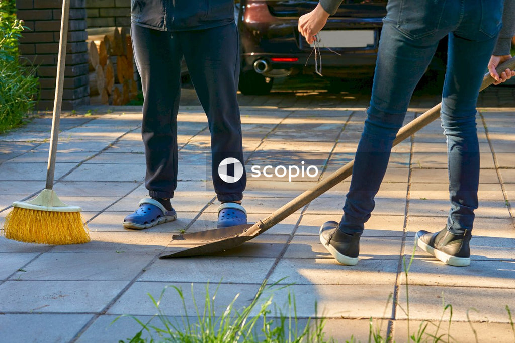 Legs of a man and a woman cleaning the house yard  with a shovel and a broom