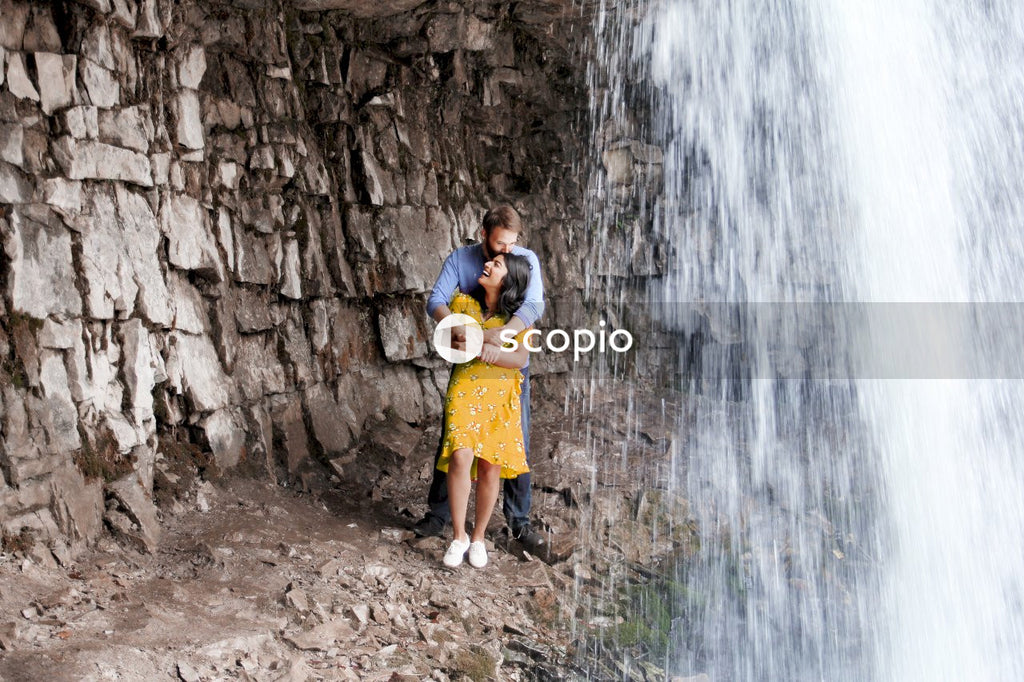 Man and woman hugging each other standing beside waterfall
