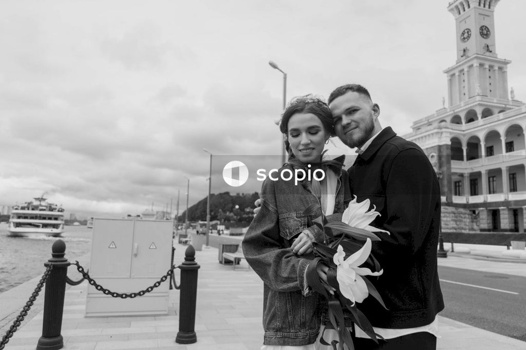 Man and woman in black suit standing near body of water in grayscale