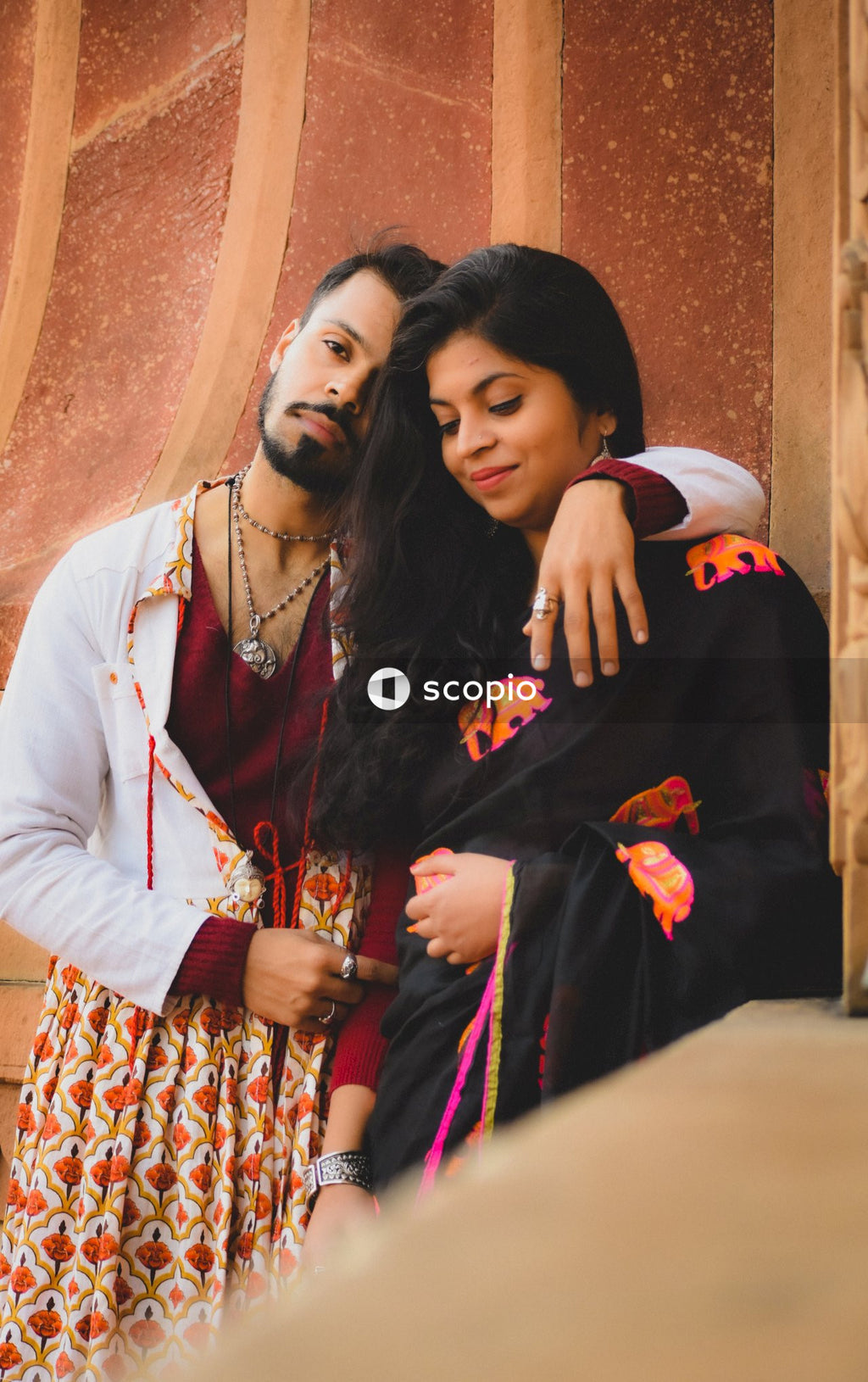 Man and woman in traditional outfits leaning on each other and standing beside a building