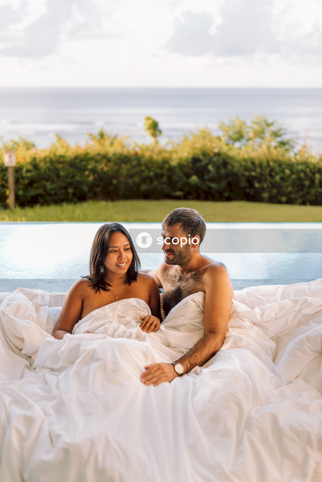 Topless man and woman under sheet beside outdoor pool