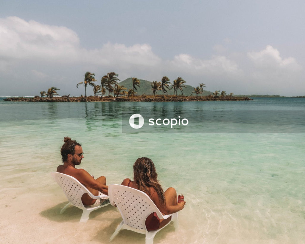 Man and woman sitting on chairs on shallow water of seashore with palm trees at distance