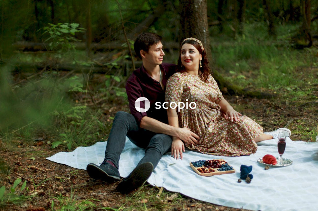 Man and woman sitting on white and blue textile surrounded by green trees