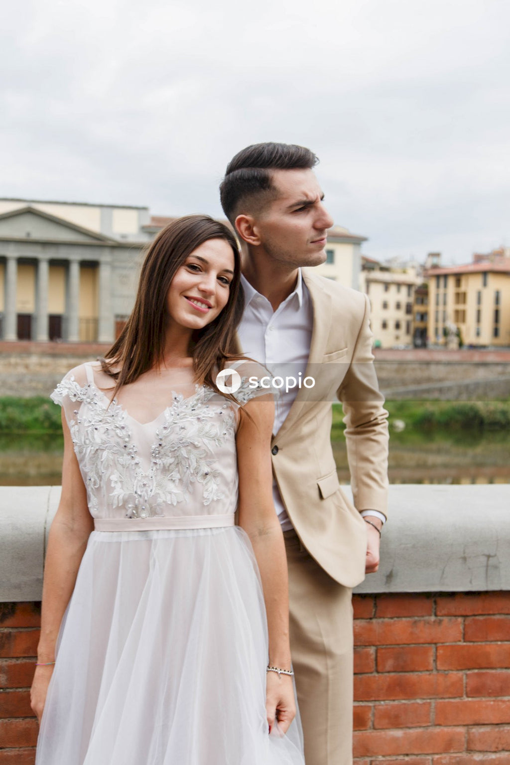 Man in beige suit jacket hugging woman in white dress