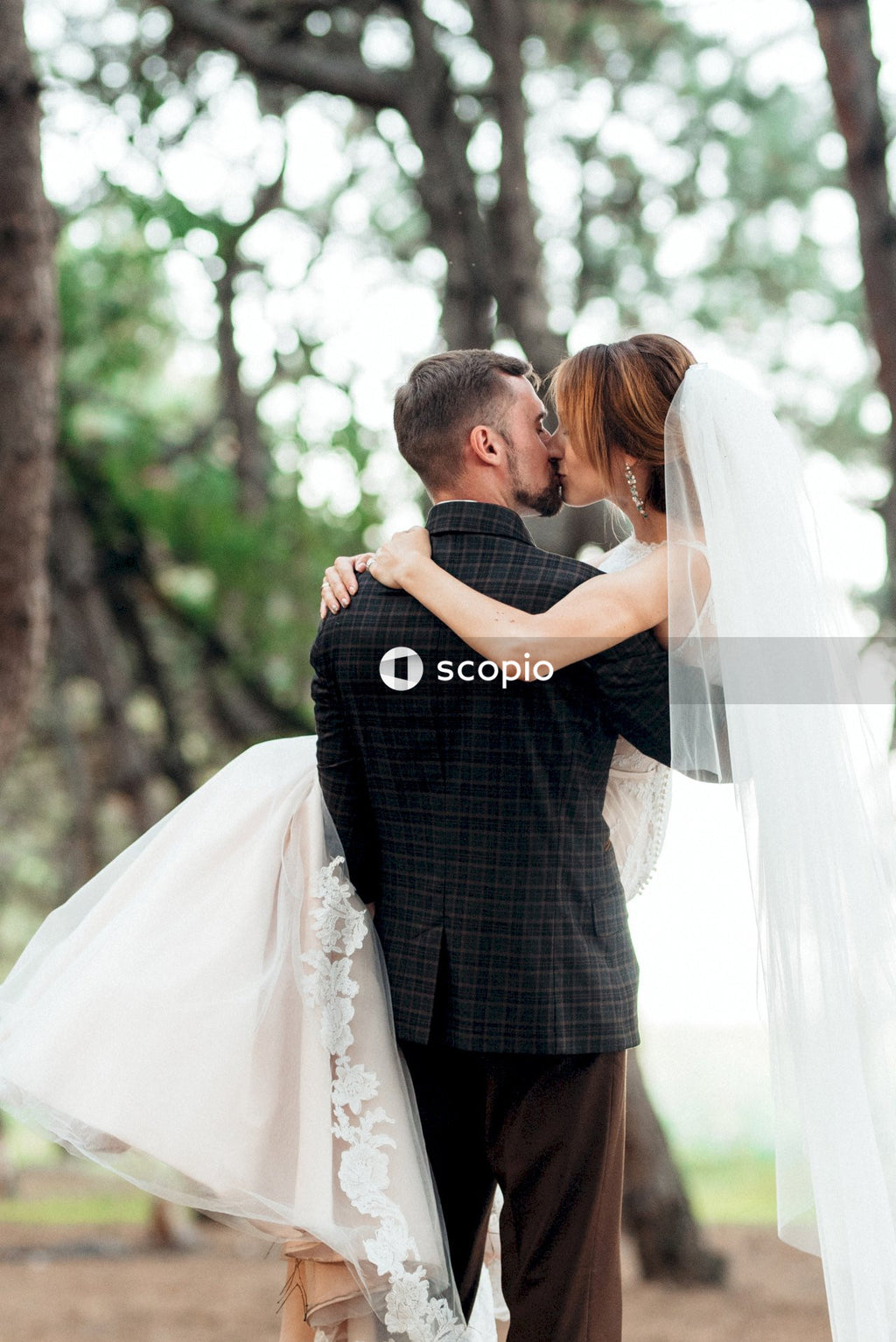 Man in black and white checked dress shirt hugging woman in white wedding gown
