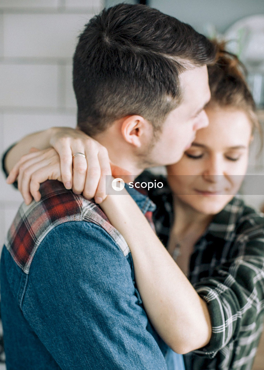 Man in black and white plaid shirt hugging woman in blue denim jeans
