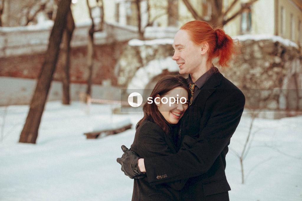 Man in black coat hugging woman in black coat on snow covered ground