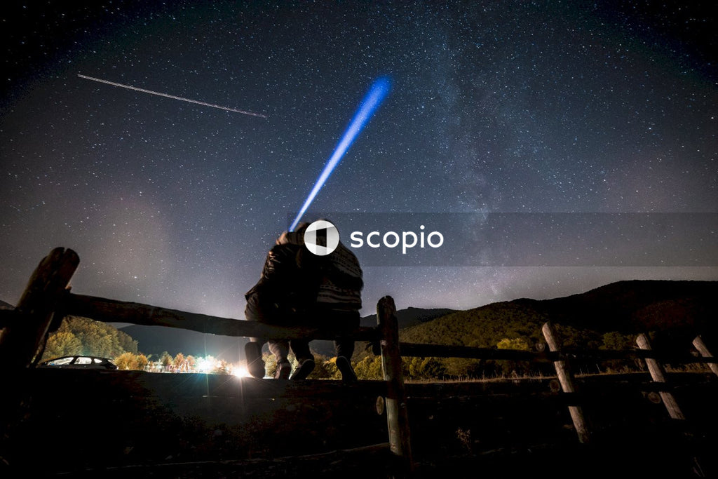 Couple hugging and sitting on wooden rail looking at starry night sky