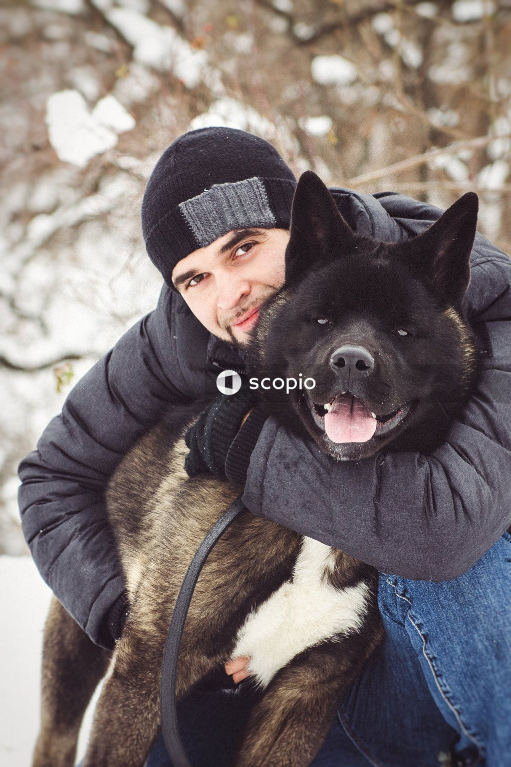 Man in black jacket hugging black and brown short coated dog