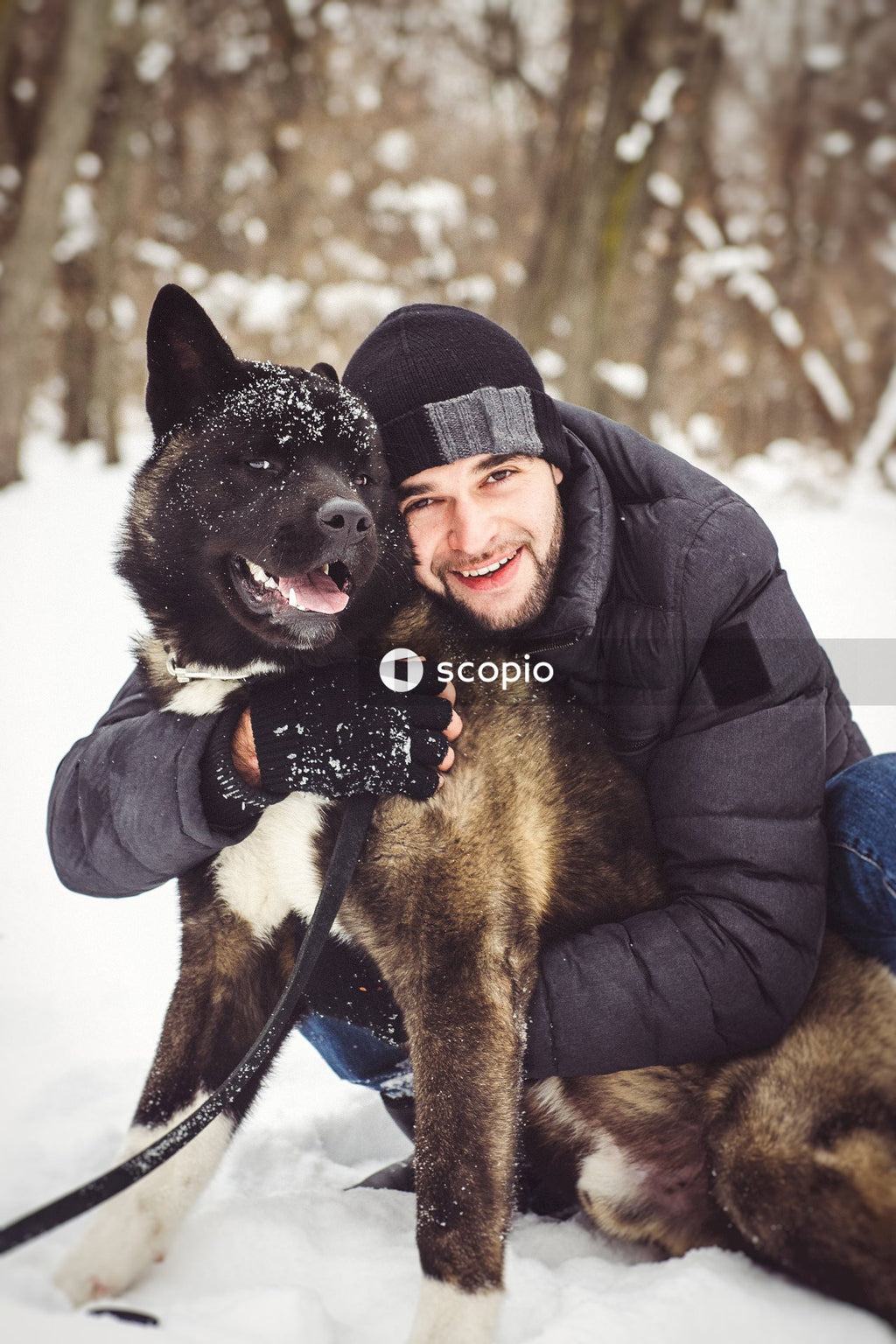 Man in black jacket hugging black and brown short coated dog on snow covered ground