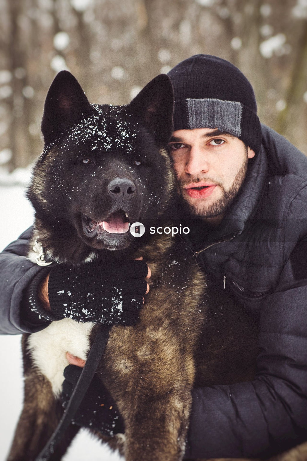 Man in black jacket hugging black and white short coated dog