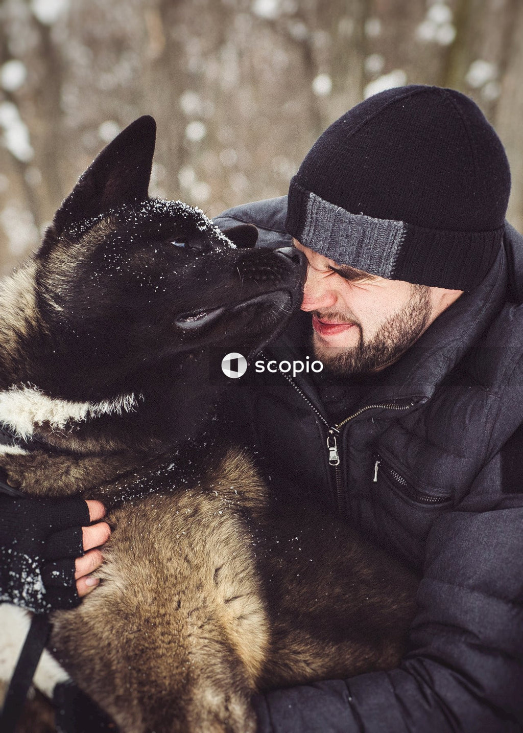 Man in black jacket hugging brown and black short coated dog