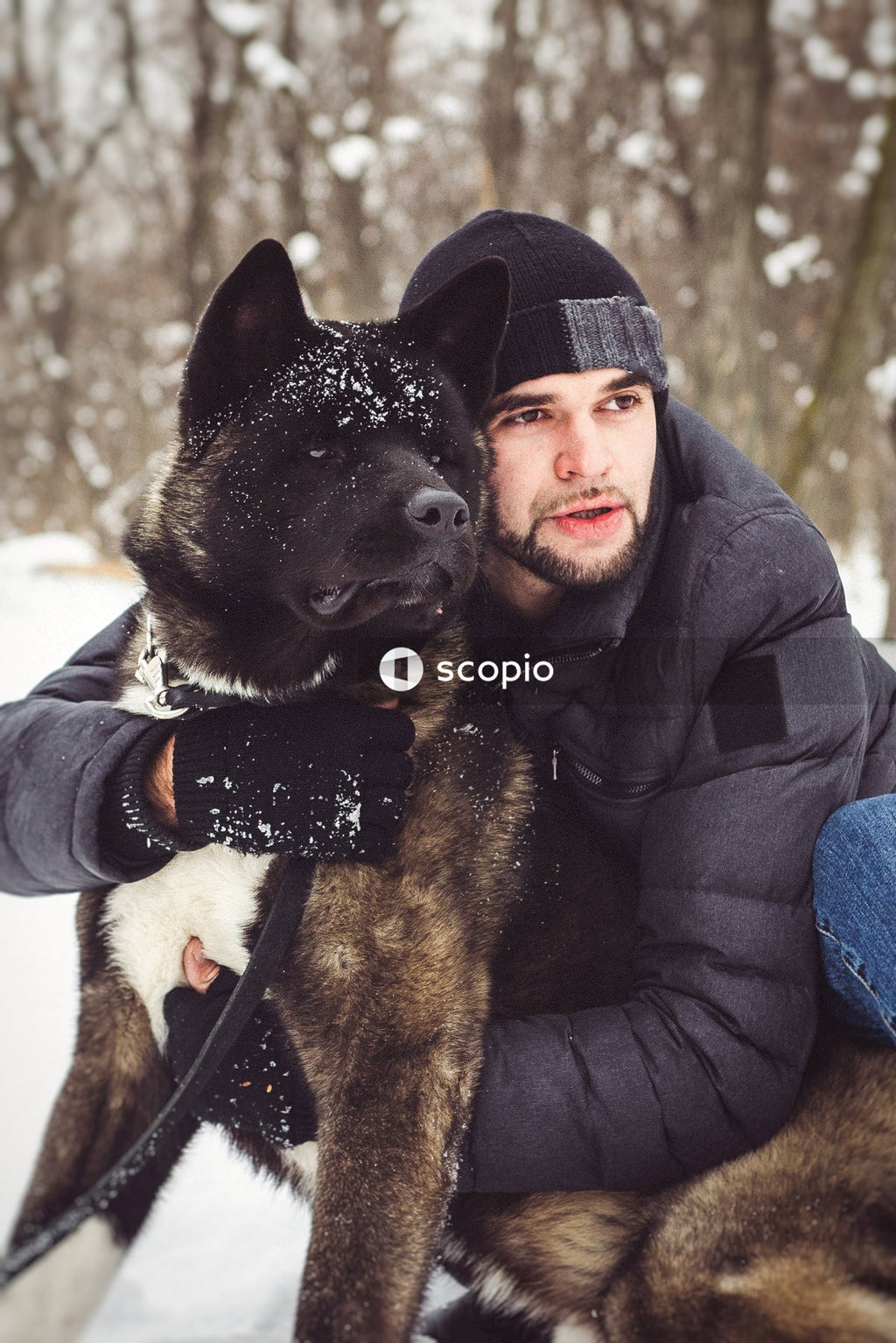 Man in black jacket hugging brown and black short coated dog