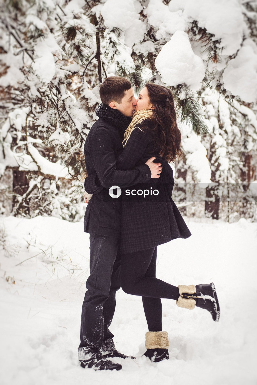 Man in black jacket hugging woman in black coat on snow covered ground