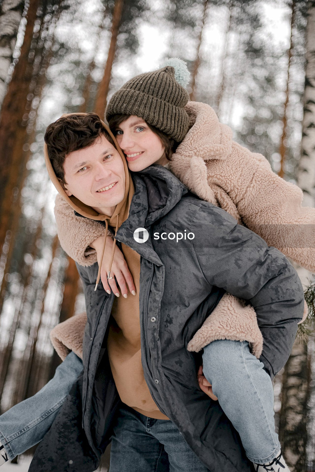 Young woman riding man's back in snow covered woods