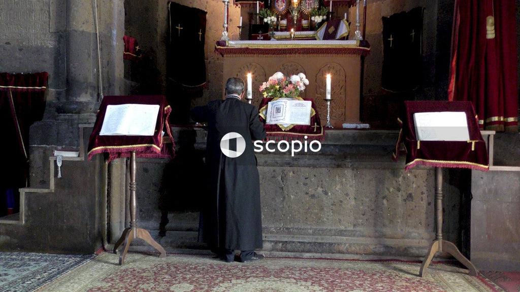 Man in black robe standing near brown wooden table