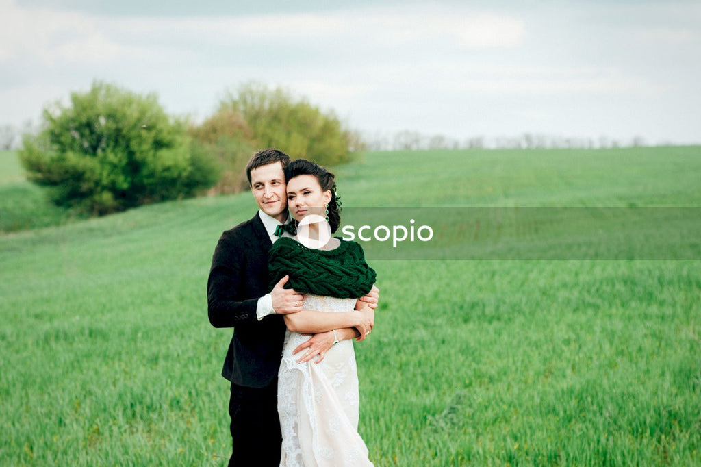 Man in black suit hugging woman in white dress on green grass field