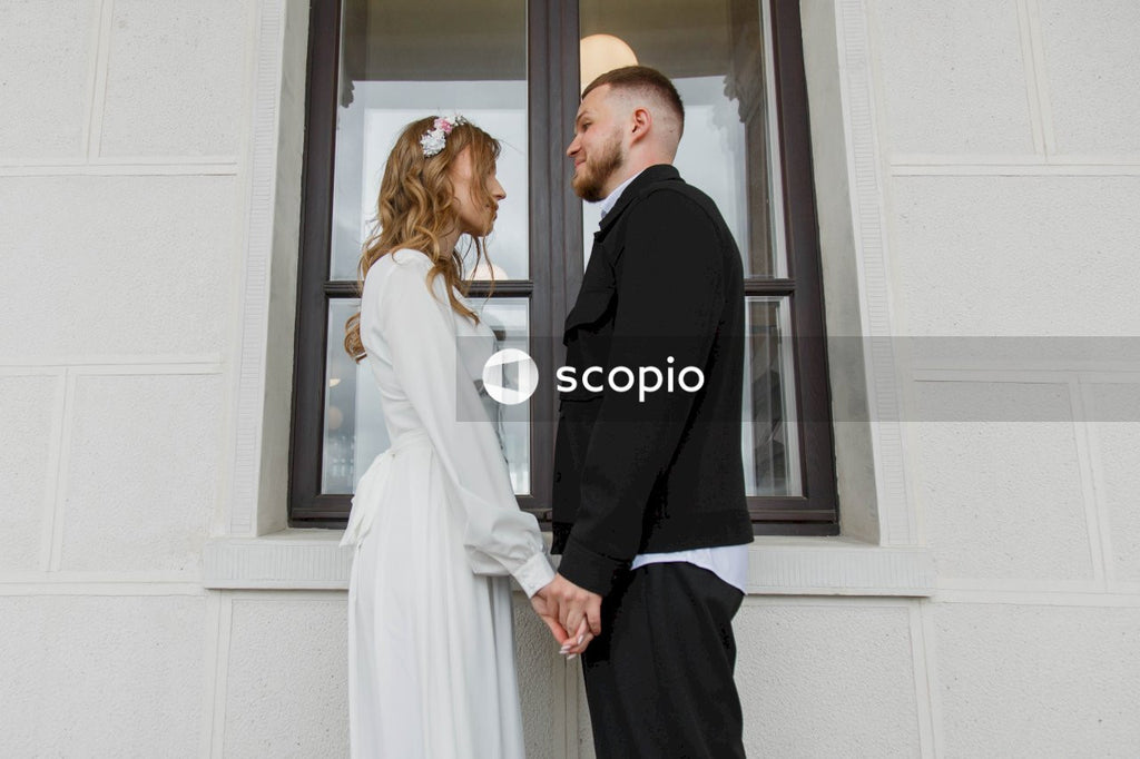Man in black suit jacket and woman in white dress standing near window