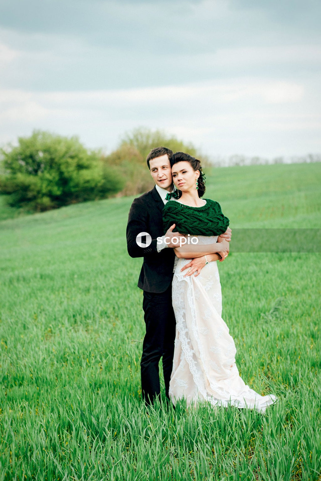 Man in black suit jacket hugging woman in white dress on green grass field