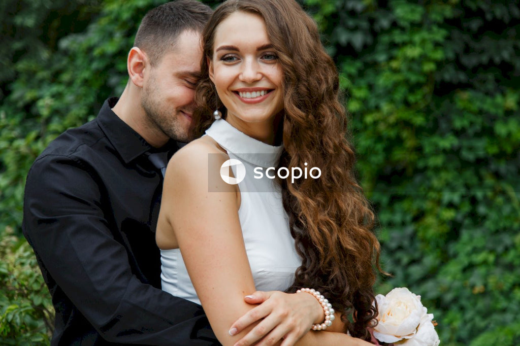 Man in black suit jacket hugging woman in white sleeveless dress