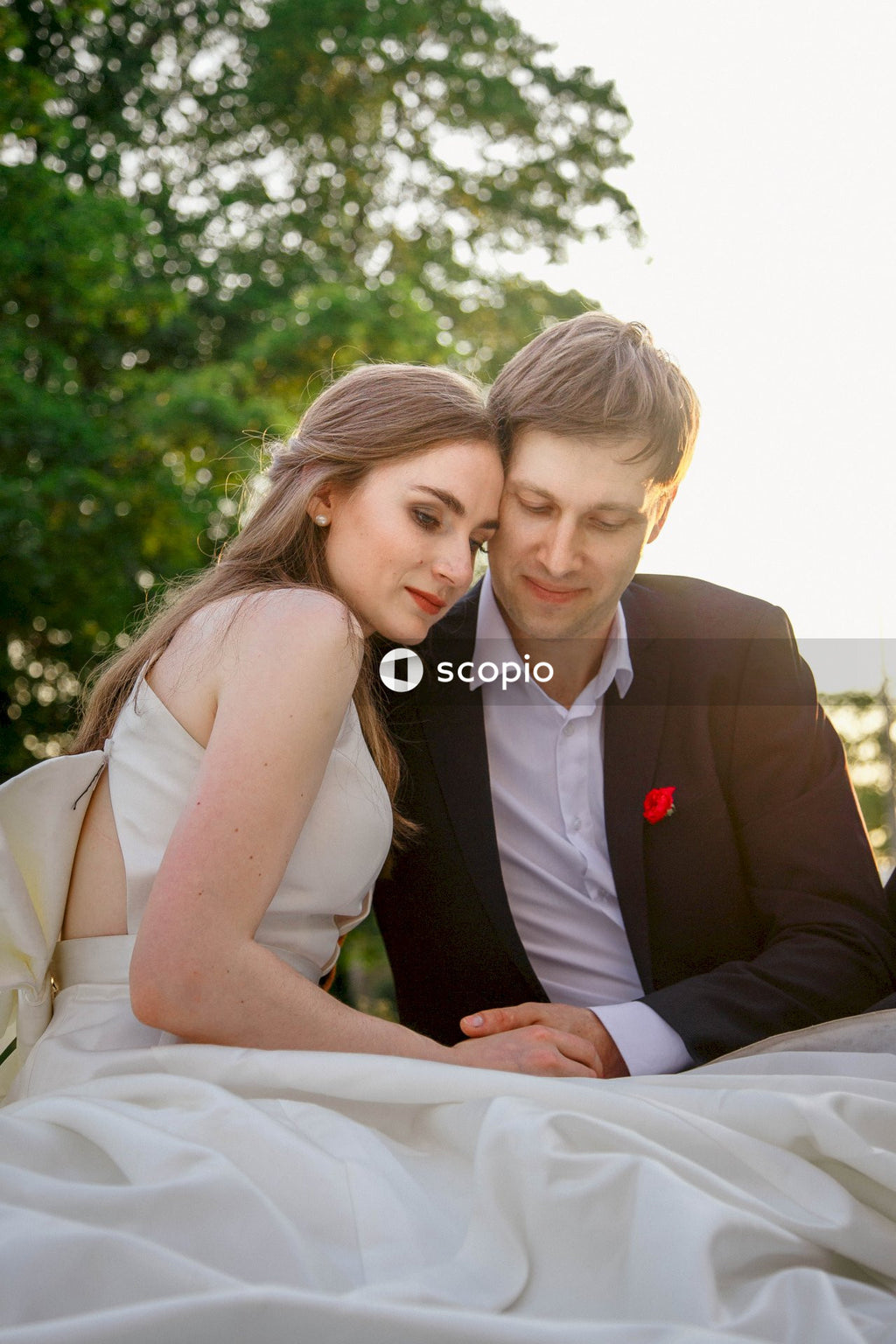 Man in black suit jacket hugging woman in white sleeveless dress