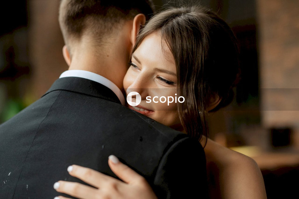 Man in black suit jacket hugging woman in white sleeveless top