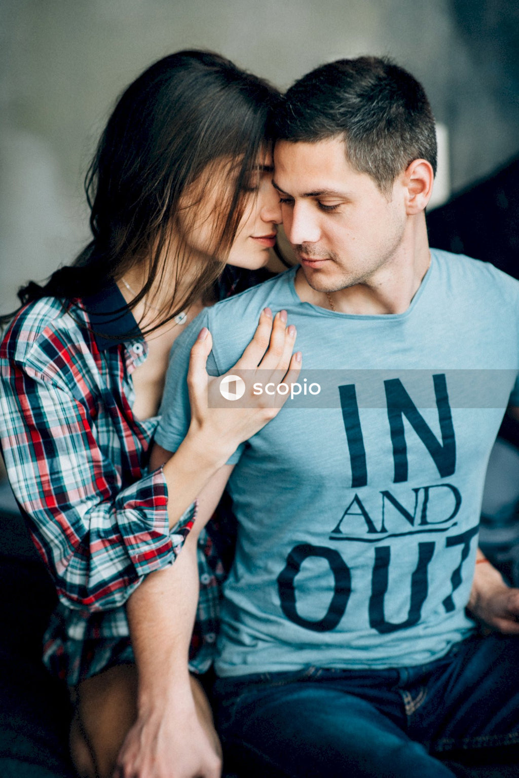 Man in blue crew neck t-shirt hugging woman in red and white plaid dress shirt
