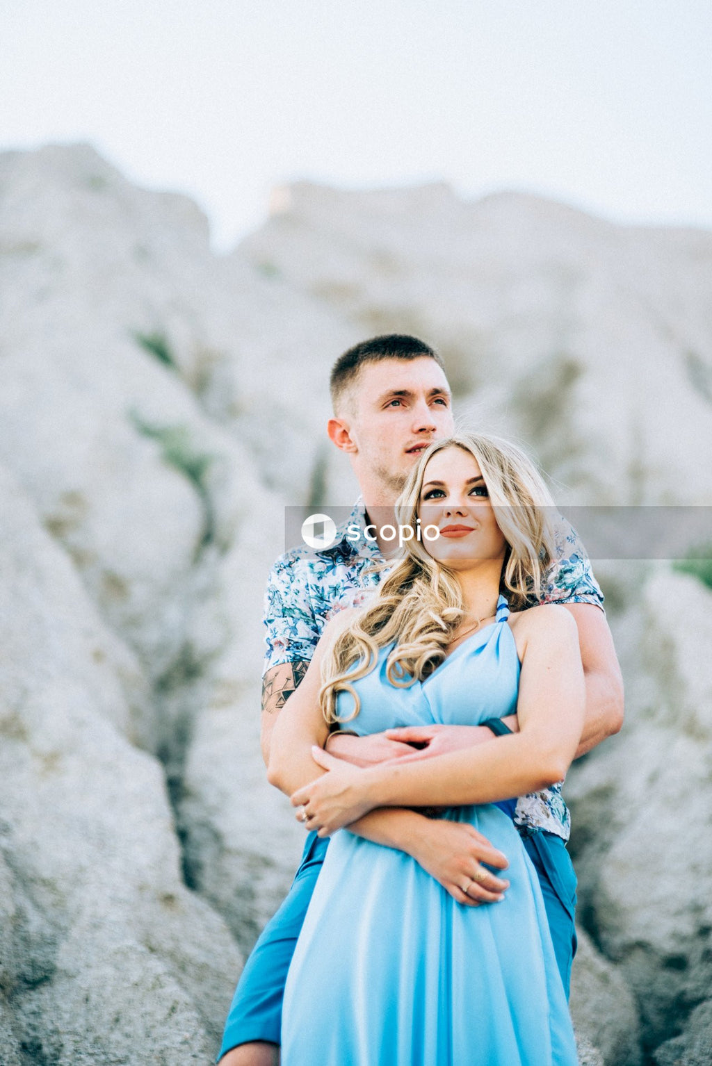 Man in blue tank top hugging woman in white and black floral sleeveless dress